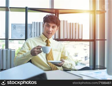 Happy young asian businessman in formal drink coffee sitting in modern workplace in break time