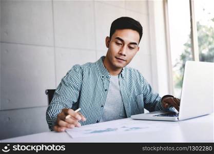 Happy Young Asian Businessman Working on Computer Laptop in his Workplace