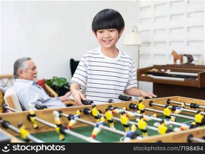 happy young asian child play football amp board at home with grandfather in background, happy family have leisure time together on weekend at home.