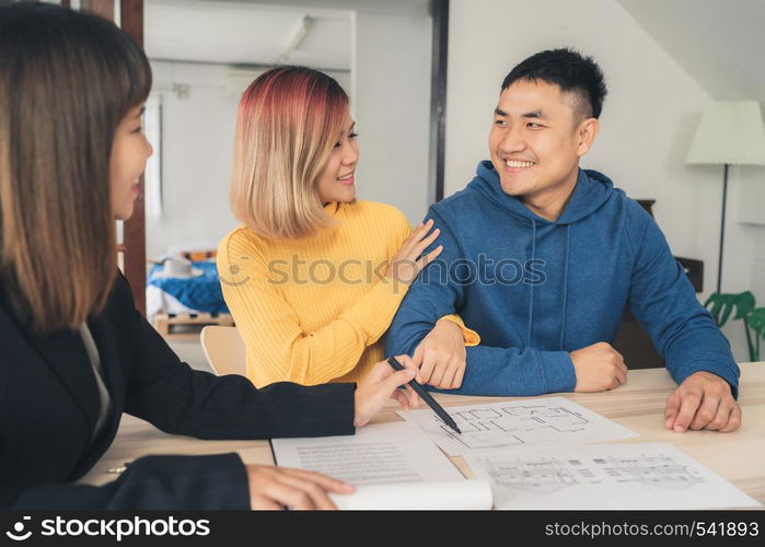 Happy young Asian couple and realtor agent. Cheerful young man signing some documents while sitting at desk together with his wife. Buying new house real estate. Signing good condition contract.