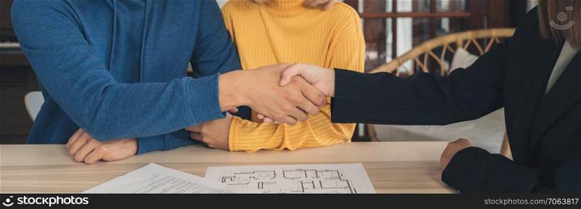 Happy young Asian couple and realtor agent. Cheerful young man signing some documents and handshaking with broker while sitting at desk. Signing good condition contract.  Panoramic banner background.