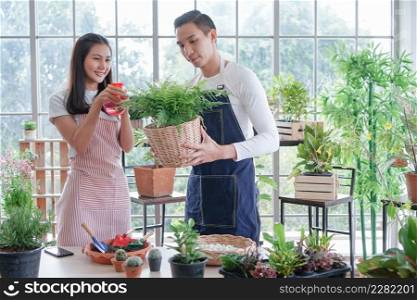 Happy young Asian couple in apron are planting plants in pots and watering plant by spray bottle in shop together