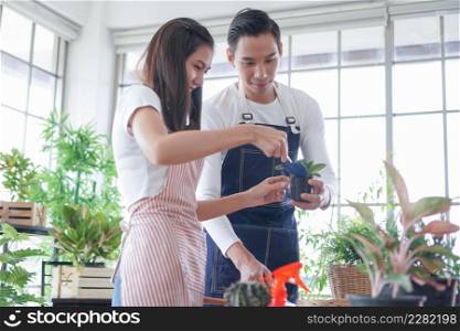 Happy young Asian couple in apron are planting plants in pots shoveling soil looking after plants in shop together