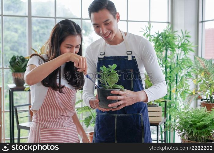 Happy young Asian couple in apron are planting plants in pots shoveling soil looking after plants in shop together