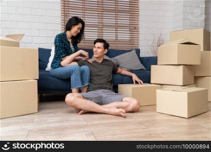 Happy young Asian couple sitting on the sofa for rest after moving to a new house on the first day. Concept of starting a new life for a newly married couple.