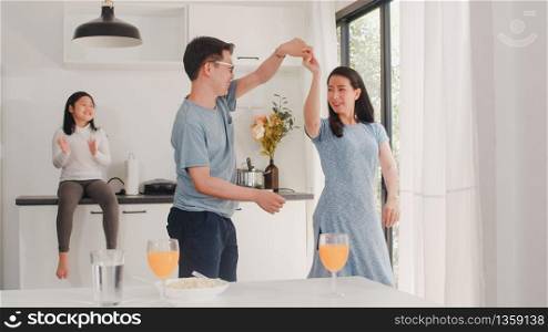Happy young Asian family listen to music and dancing after breakfast at home. Attractive Japanese mother father and child daughter are enjoying spending time together in modern kitchen in the morning.