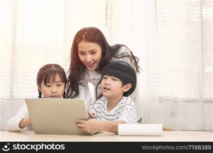 Happy young Asian family with children and their mother using computer do school homework at home.