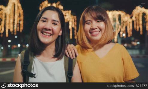 Happy young Asian girls couple tourist with casual style smiling looking at camera peaceful picture of background in city street at night. Lifestyle tourist travel holiday concept.