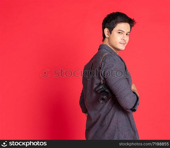 Happy young asian hipster photographer man in casual fashion using vintage camera freedom lifestyle travel concept isolated on red background studio shot.