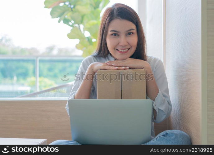 Happy young Asian woman entrepreneur, Hold package and Smile for sale success of online shopping store at home office, Concept of merchant, small business, online business and eCommerce.