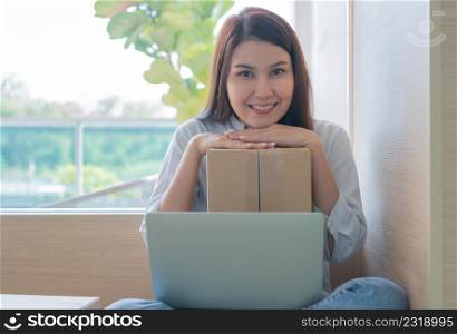 Happy young Asian woman entrepreneur, Hold package and Smile for sale success of online shopping store at home office, Concept of merchant, small business, online business and eCommerce.