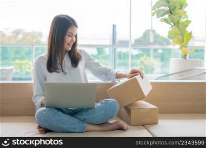 Happy young Asian woman entrepreneur, Hold package and Smile for sale success of online shopping store at home office, Concept of merchant, small business, online business and eCommerce.