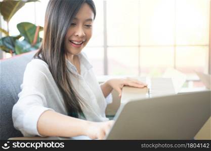 Happy young Asian woman entrepreneur, Smile for sales success after checking order from online shopping store in laptop at home office, Concept of merchant business online and eCommerce