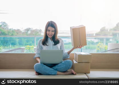 Happy young Asian woman entrepreneur, Smile for sales success after checking order from online shopping store in a laptop at home office, Concept of merchant business online and eCommerce