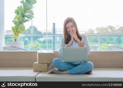 Happy young Asian woman entrepreneur, Smile for sales success after checking order from online shopping store in a laptop at home office, Concept of merchant business online and eCommerce