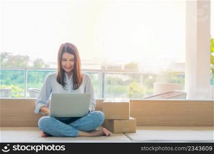 Happy young Asian woman entrepreneur, Smile for sales success after checking order from online shopping store in a laptop at home office, Concept of merchant business online and eCommerce