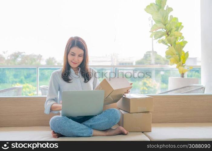 Happy young Asian woman entrepreneur, Smile for sales success after checking order from online shopping store in a laptop at home office, Concept of merchant business online and eCommerce