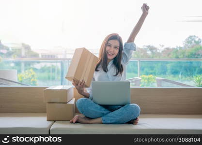 Happy young Asian woman entrepreneur, Smile for sales success after checking order from online shopping store in a laptop at home office, Concept of merchant business online and eCommerce