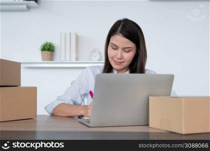 Happy young Asian woman entrepreneur, Take note after check order and Smile for sale success of online shopping store, Concept of the merchant, small business, online business, and eCommerce.