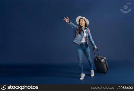 Happy young Asian woman holding  baggage and hurry up to airport on blue color background, carry backpacker and wearing headphone, holiday and vacation, travel and tourist concept