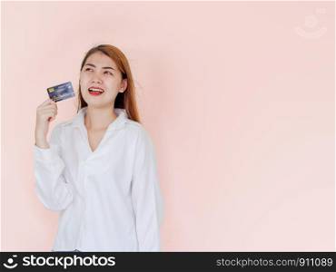 Happy young asian woman holding credit card in hand with smiling face and feeling excited for use card to make everyday purchases, restaurants or shop online. studio shot isolated on pink background