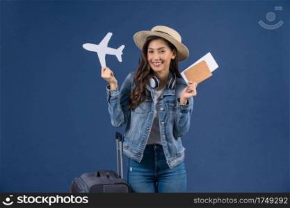 Happy young Asian woman holding passport with boarding pass and airplane mockkup white paper on blue color background, holiday and travel concept