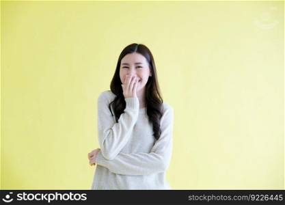 Happy young asian woman laughing while standing over isolated yellow background