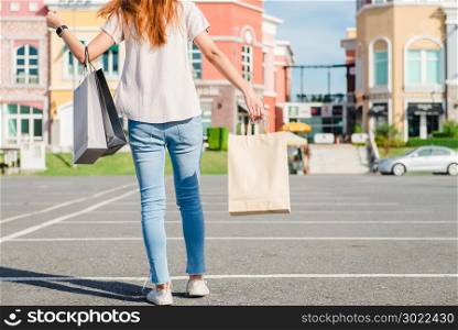 Happy young Asian woman shopping an outdoor market with a background of pastel buildings and blue sky. Young woman smile with a colorful bag in her hand. Outdoor shopping concept.