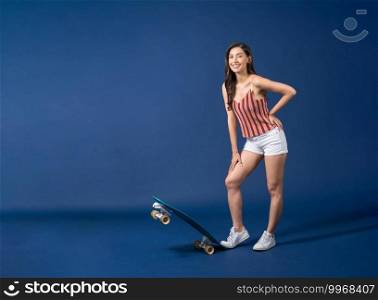 Happy young Asian woman standing on surfskate or skateboard on blue color background, exercise and sport, trendy and extream sports concept
