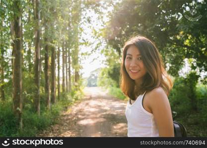 Happy young Asian woman traveler with backpack walking in forest. Hiker Asian woman with backpack walking on path in summer forest. Adventure backpacker travel people concept.
