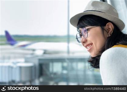 Happy Young Asian woman wear eyeglasses and hat with a beautiful smile is enjoying in her trip at the airport. Looking away. Positive emotion.