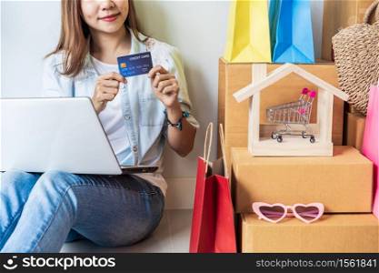 Happy young asian woman with colorful shopping bag, fashion items and stack of cardboard boxes at home, Using credit card for online shopping concept