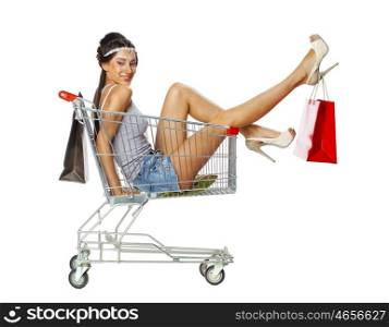 Happy young beautiful brunette woman sits in an empty shopping cart with a red bag, isolated on white background