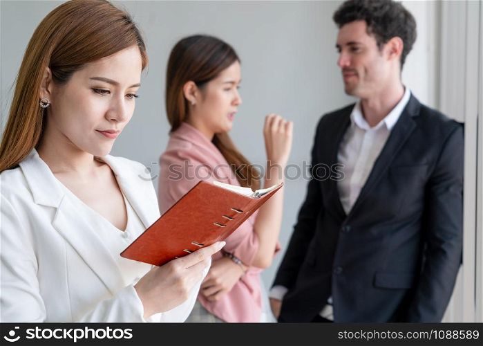 Happy young beautiful businesswoman reading book and working in office with colleagues and friend at workplace. Corporate business people group.