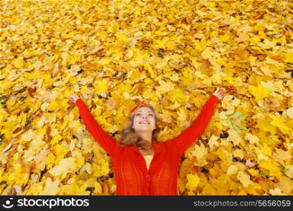 Happy young beautiful woman laying on dry autumn leaves