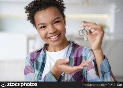 Happy young biracial girl showing key to new home, first house, apartment, looking at camera. Smiling mixed race female houseowner renter tenant holding bunch of keys. Real estate agency advertisement. Smiling young biracial girl houseowner tenant holds house key to new home. Real estate service