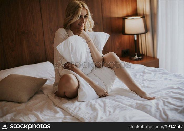 Happy young blonde woman hugging her pillow at home in the bedroom