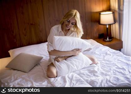 Happy young blonde woman hugging her pillow at home in the bedroom