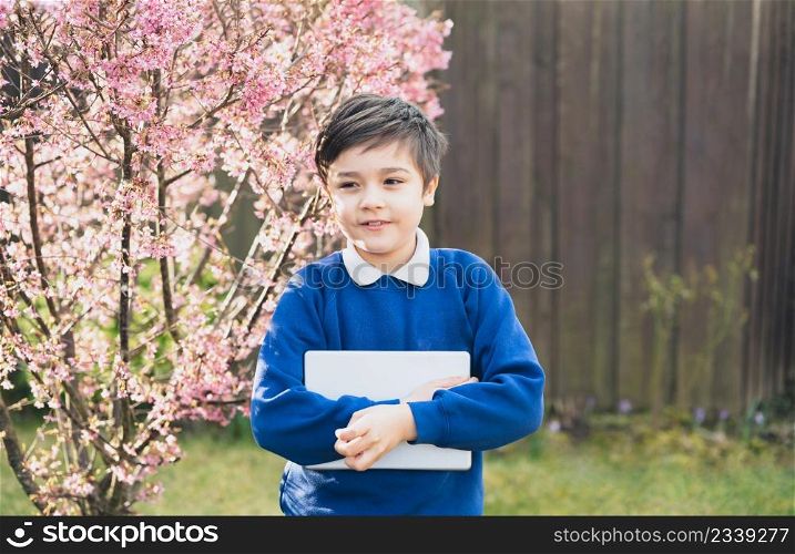 Happy young boy holding tablet pc standing outside waiting for School bus, Portrait Kid with smiling face standing alone in the front garden, Preschool boy learning with modern technology