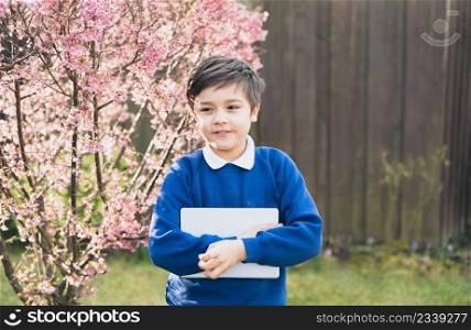 Happy young boy holding tablet pc standing outside waiting for School bus, Portrait Kid with smiling face standing alone in the front garden, Preschool boy learning with modern technology