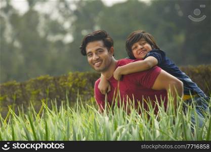 Happy young boy piggy riding on the back of his father outdoors with fresh grass in the foreground.