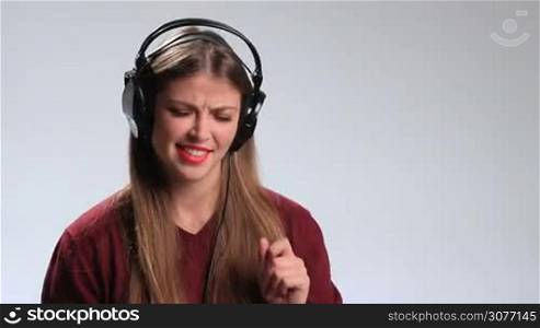 Happy young brunette woman with big headphones listening track on mp3 player. Crazy expressive hipster girl in cheerful mood enjoying her favorite upbeat song in earphones, gesturing, swaying along with the music, making funny face.