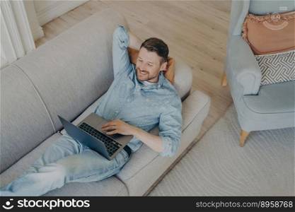 Happy young business company worker in casual clothes relaxing and smiling with confidence while lying  on couch with hand behind head after successful online presentation. Young business company worker in casual clothes relaxing after successful online presentation