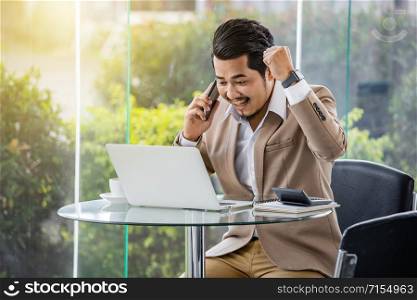 happy young business man talking on mobile phone and using laptop