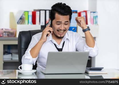 happy young business man talking on mobile phone and using laptop