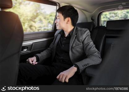happy young business man thinking and looking view out of window while sitting in the back seat of car