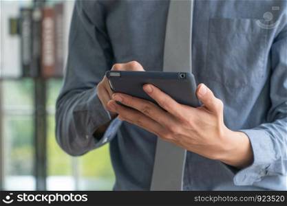 Happy young business man using digital tablet and smiling, standing near the window in office