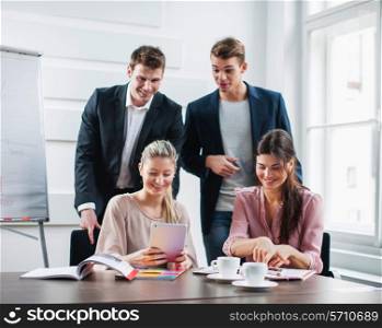 Happy young business people using tablet PC at desk in office