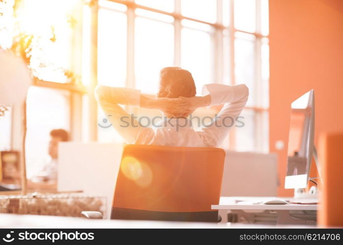 Happy young business woman relaxing and geting insiration while working on desktop computer at modern bright starup office interior. Morning sunrise or sunset with sun flare in background.
