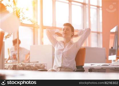 Happy young business woman relaxing and geting insiration while working on desktop computer at modern bright starup office interior. Morning sunrise or sunset with sun flare in background.